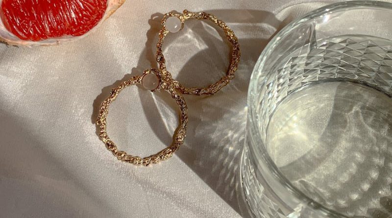 Close-up of grapefruit, gold earrings, and glass on a satin surface.