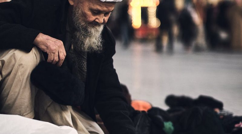 A senior man sells hats and headwear at an outdoor market, showcasing traditional attire and craftsmanship.